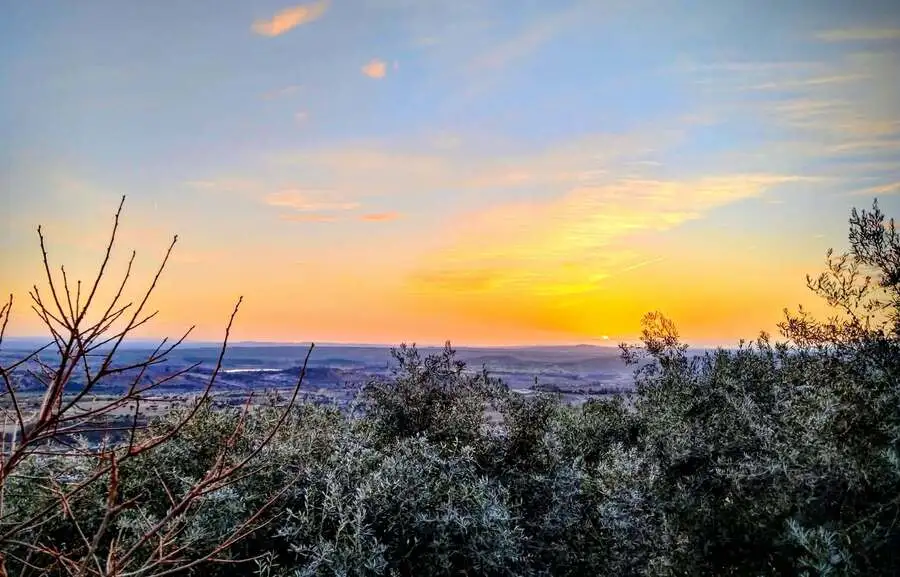 Pôr do sol com tons de laranja e amarelo no horizonte sobre uma planície vasta