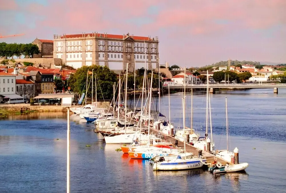Vista do imponente Convento de Santa Clara sobre o Rio Ave com barcos de recreio na marina.