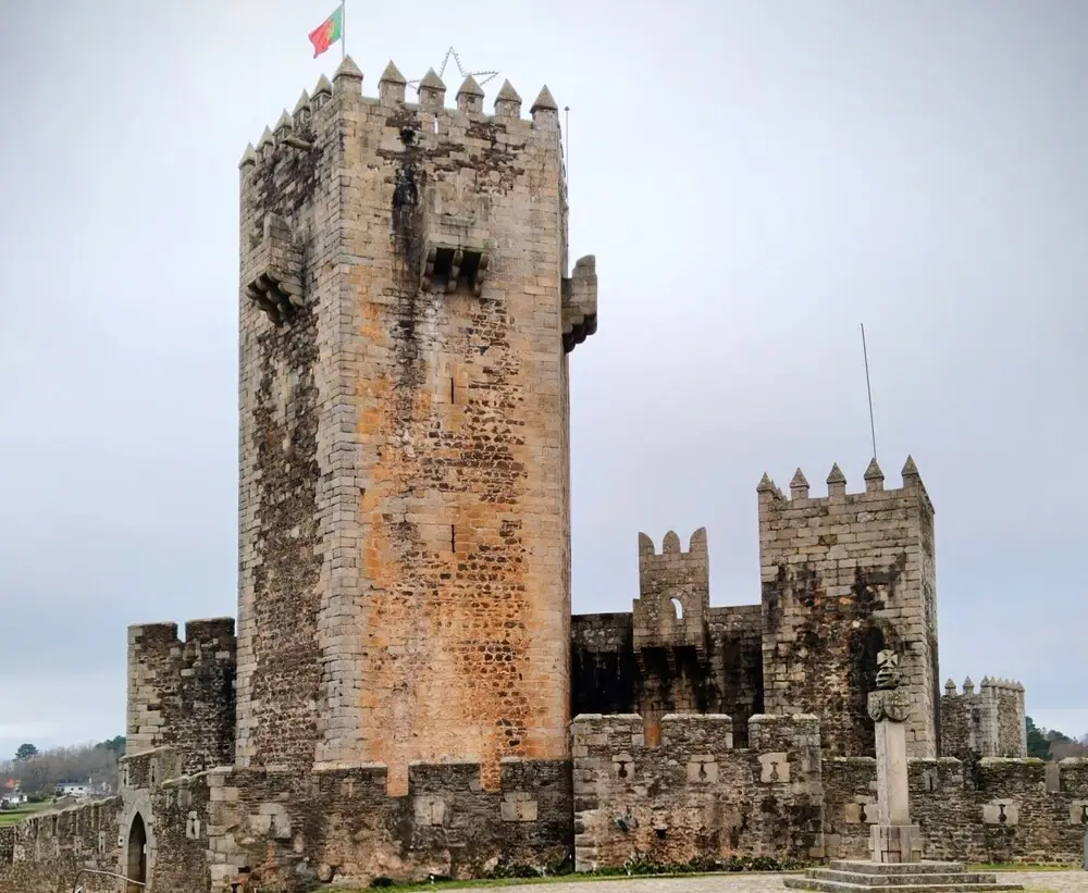 Castelo do Sabugal com torre de menagem pentagonal e muralhas medievais sob céu azul.