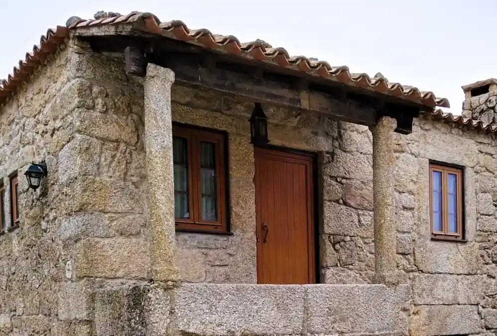 Fachada de casa tradicional em granito com varanda e colunas de pedra na Aldeia Histórica de Sortelha.