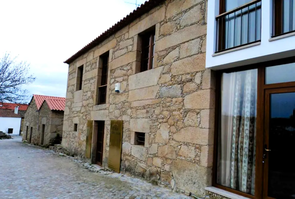 Edifício em pedra com extensão moderna envidraçada, numa aldeia típica do Sabugal, perfeito para uma estadia com ambiente tradicional.