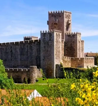 Detalhe de flores coloridas em primeiro plano com as muralhas e torres do Castelo do Sabugal desfocadas ao fundo.