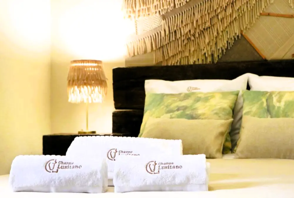 Cama preparada com almofadas e toalhas bordadas, num quarto confortável e bem iluminado em casa de campo Inguias.