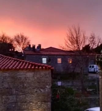 Entardecer com céu rosado sobre o pelourinho e casas medievais em Sortelha.