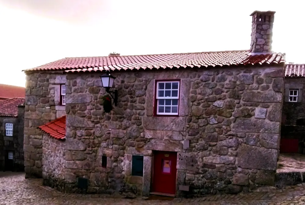 Fachada de casa de granito com janela manuelina e porta vermelha em Sortelha.
