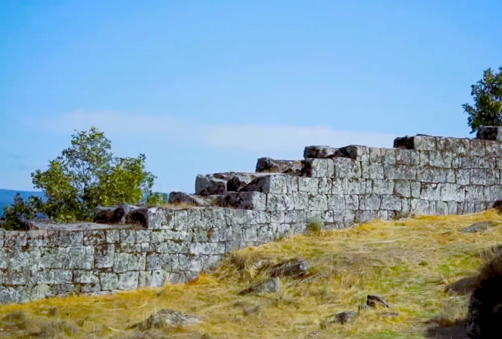 Fileiras de muralhas defensivas em degraus feitas de pedra sobre uma colina gramada em Vila do Touro.