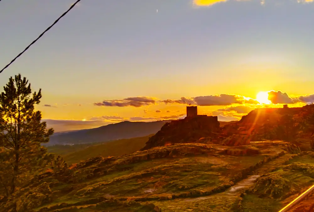 Silhueta do Castelo de Sortelha ao pôr do sol com luz dourada sobre as muralhas medievais.
