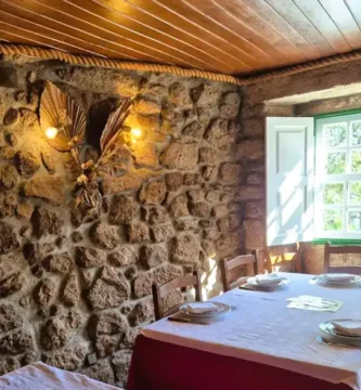 Interior rústico do Restaurante Dom Sancho em Sortelha com paredes de pedra granito, janela de madeira e mesa posta.