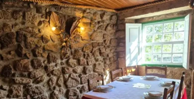 Interior rústico do Restaurante Dom Sancho em Sortelha com paredes de pedra granito, janela de madeira e mesa posta.