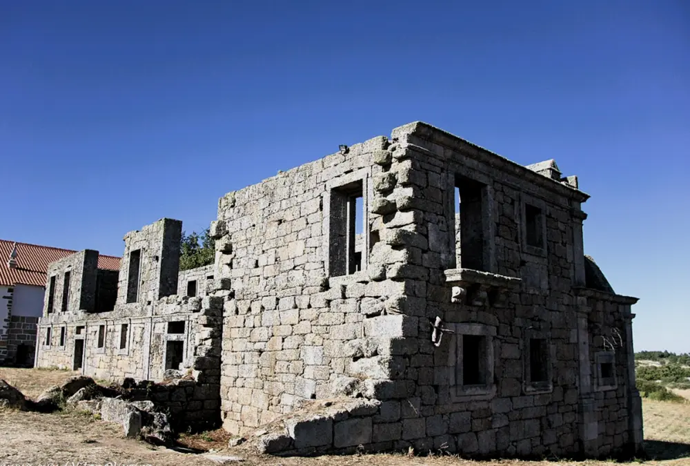 Ruínas em granito do antigo Santuário e Convento de Sacaparte, mostrando as janelas retangulares e as paredes robustas de pedra contra um céu azul.