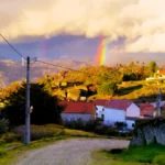 Arco-íris sobre a paisagem rural e casas de telhado vermelho em Sortelha, Portugal.
