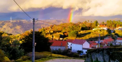 Arco-íris sobre a paisagem rural e casas de telhado vermelho em Sortelha, Portugal.
