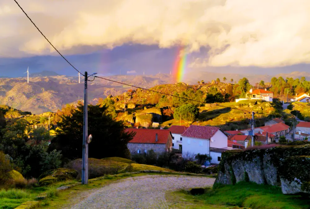 Arco-íris sobre a paisagem rural e casas de telhado vermelho em Sortelha, Portugal.