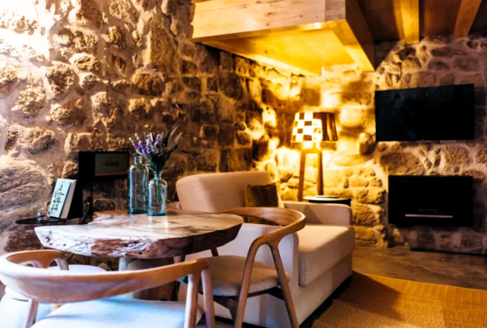 Sala com paredes de pedra, mobiliário contemporâneo e iluminação quente, num alojamento rural de Sortelha