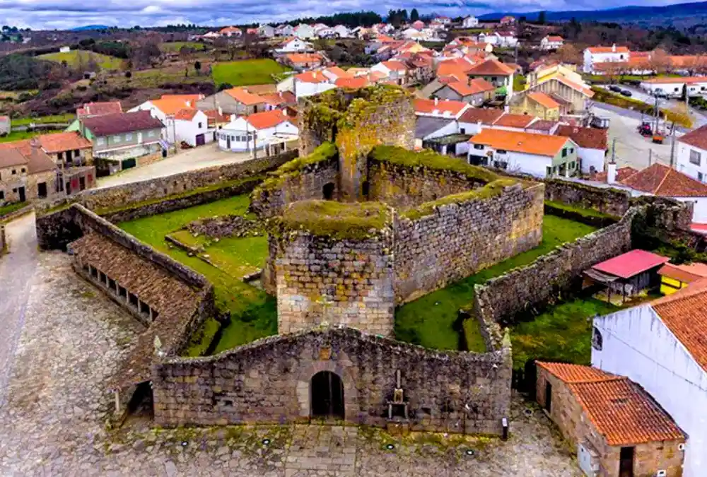 Vista aérea do Castelo de Alfaiates evidenciando a sua planta quadrangular, as muralhas de pedra cobertas de musgo e a envolvente das casas da vila.