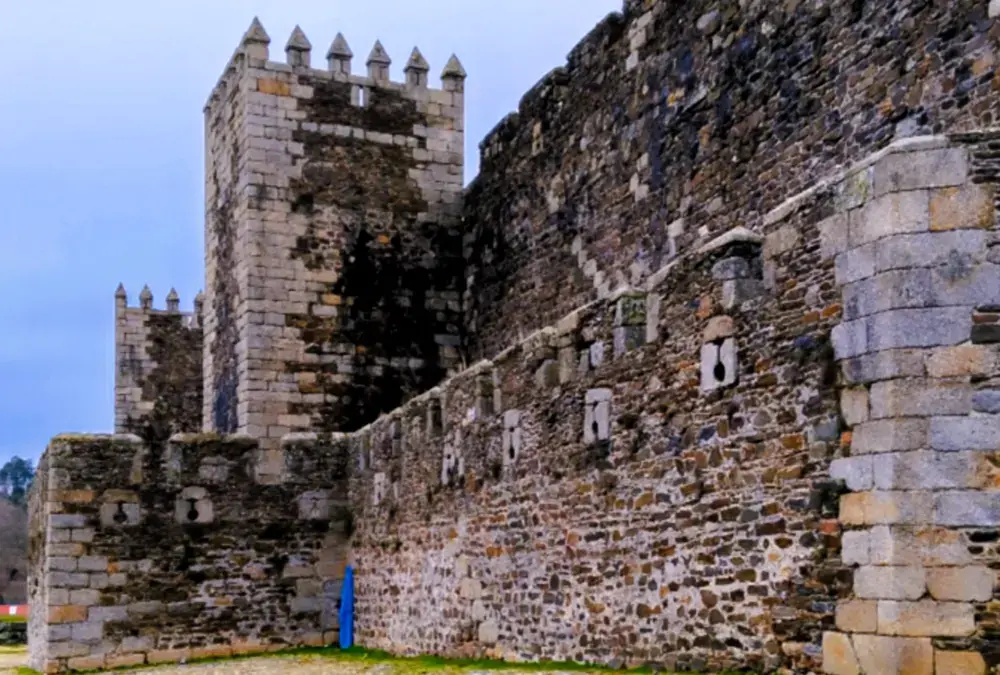Vista lateral externa do Castelo do Sabugal com chão de pedra irregular e céu nublado.