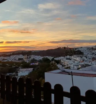 Vista panorâmica de Arcos de la Frontera ao pôr do sol, mostrando o casario branco empilhado na colina sob um céu com tons dourados e azulados.
