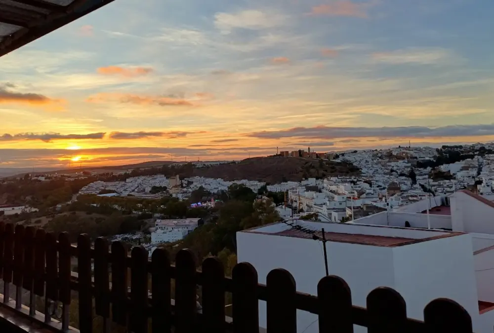 Vista panorâmica de Arcos de la Frontera ao pôr do sol, mostrando o casario branco empilhado na colina sob um céu com tons dourados e azulados.