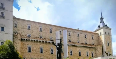 Fachada de pedra do Alcázar de Toledo com céu nublado e estátua de bronze em primeiro plano.