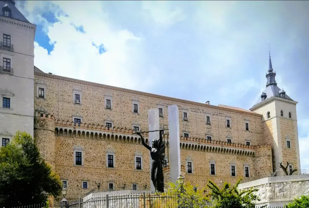 Fachada de pedra do Alcázar de Toledo com céu nublado e estátua de bronze em primeiro plano.
