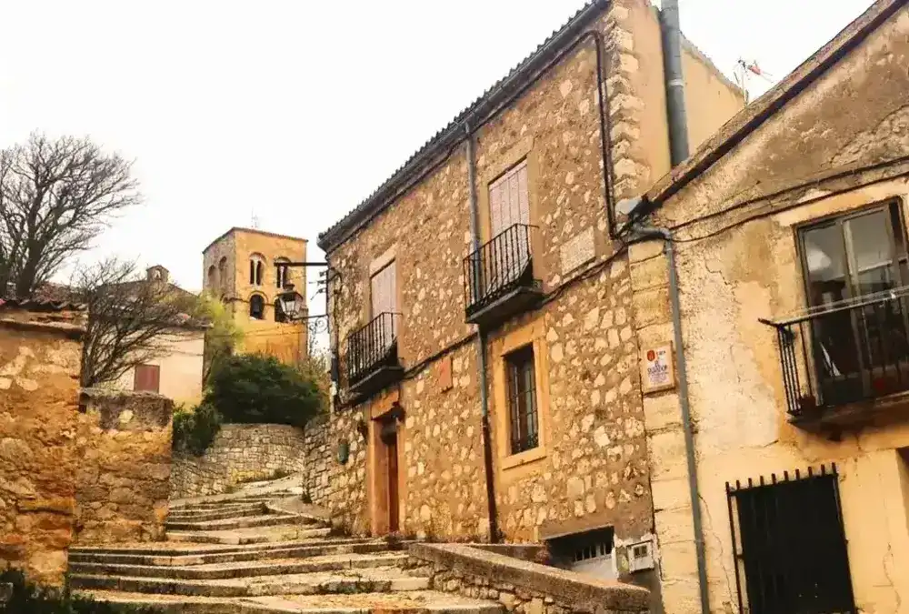 Rua medieval de Sepúlveda em subida com escadas de pedra e torre de igreja românica ao fundo, Segóvia.