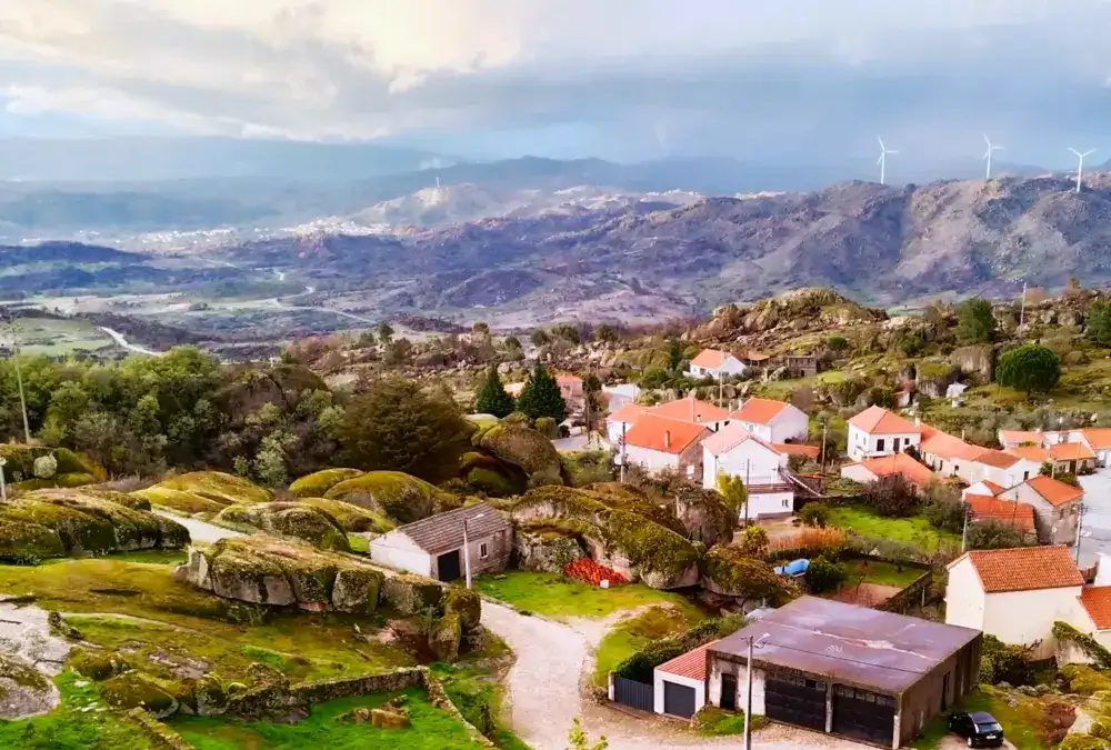 Vista aérea das casas típicas de Sortelha com telhados laranjas e aerogeradores ao fundo.