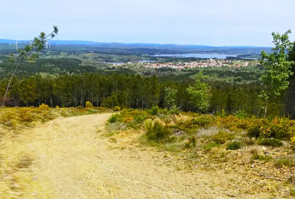 Vista panorâmica de um trilho no Sabugal com a Albufeira da Meimoa ao fundo sob um céu nublado.