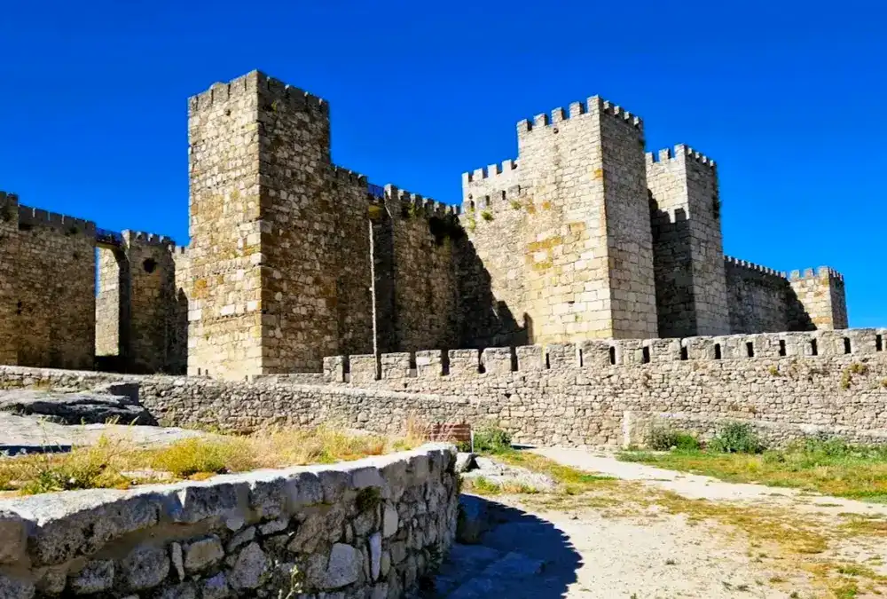 Muralhas defensivas em granito do Castelo de Trujillo com as suas torres quadrangulares contra o céu azul.
