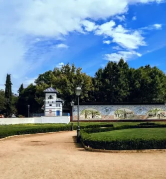 Jardim público com caminhos de terra, apresentando um longo muro decorado com painéis de azulejos artísticos de Talavera de la Reina nos Jardines del Prado.