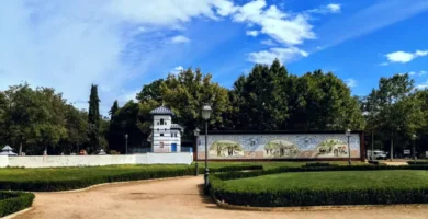 Jardim público com caminhos de terra, apresentando um longo muro decorado com painéis de azulejos artísticos de Talavera de la Reina nos Jardines del Prado.