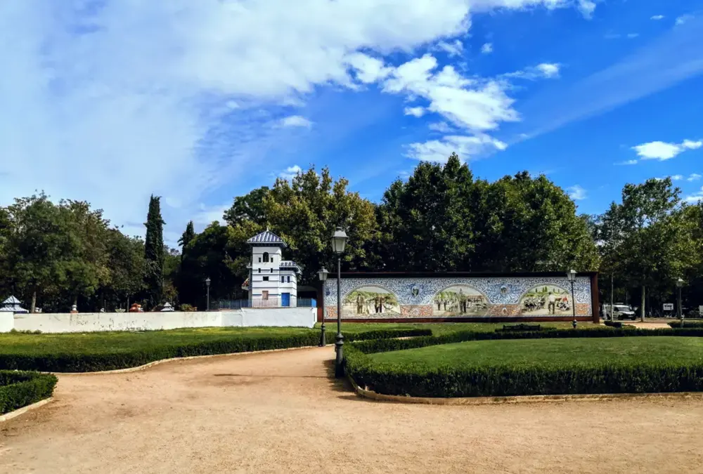 Jardim público com caminhos de terra, apresentando um longo muro decorado com painéis de azulejos artísticos de Talavera de la Reina.
