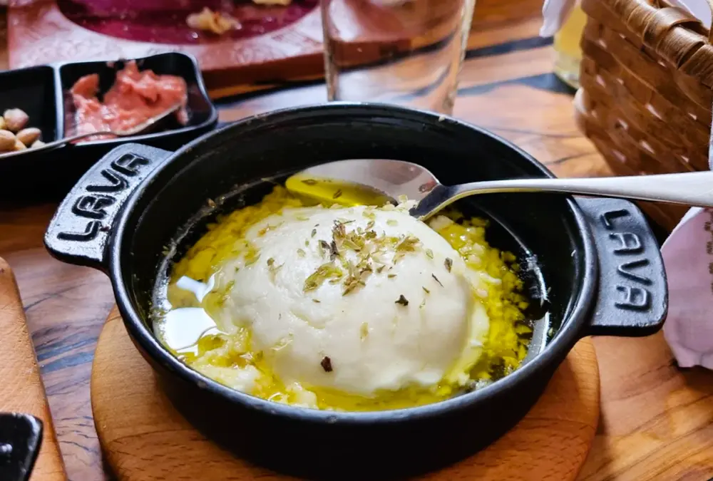 Açorda alentejana servida em panela de barro preta sobre base de madeira no Restaurante Tombalobos.