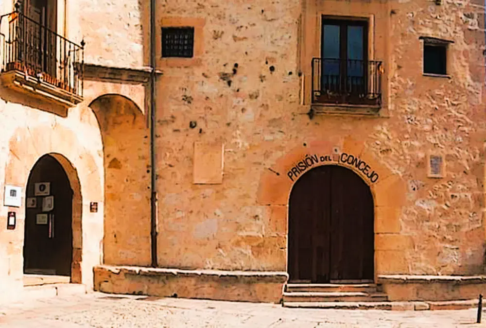 Fachada de pedra rústica da Antiga Prisão do Conselho em Sepúlveda, com um arco de entrada de pedra que tem a inscrição "PRISIÓN DEL CONCEJO" e varandas de ferro forjado.