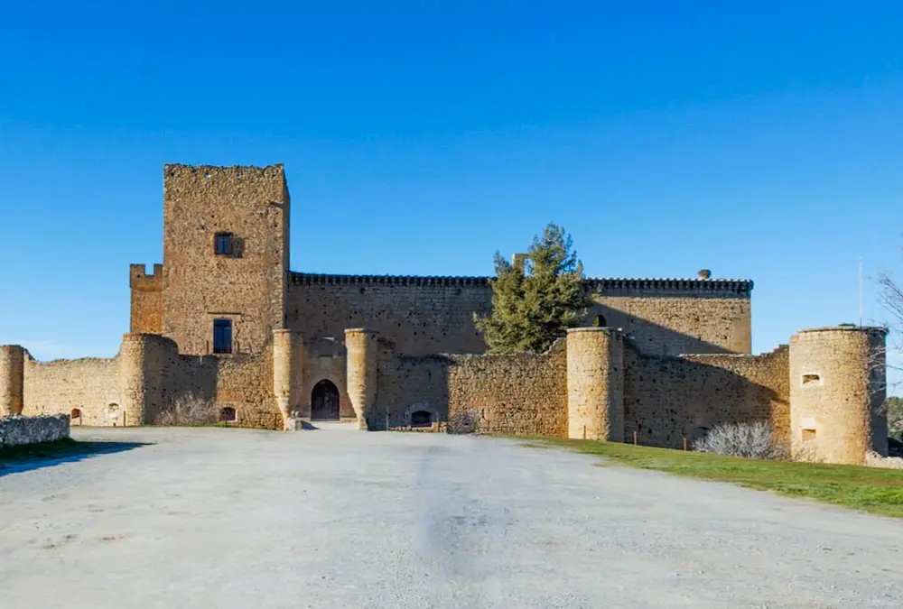 Fachada frontal do Castelo de Pedraza com a sua torre de menagem quadrada e muralhas defensivas iluminadas pelo sol.