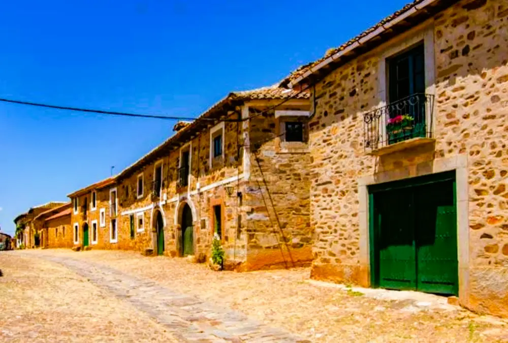 Rua de pedra histórica com casas de pedra tradicionais e portões verdes em Castrillo de los Polvazares. Lugar perfeito para viagens com crianças.