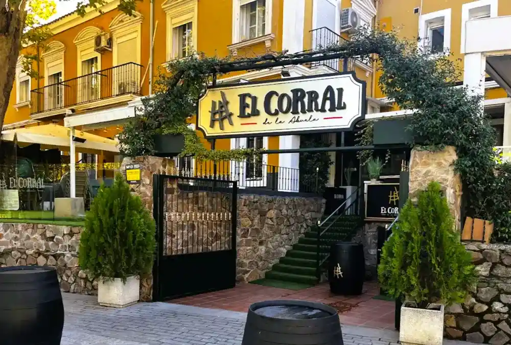 Fachada do restaurante El Corral de la Abuela em Aranjuez com arco de vegetação e barris decorativos.