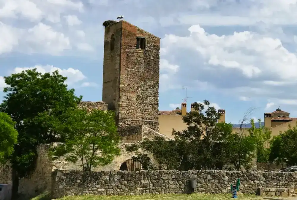 Torre sineira românica da Igreja de Santa Maria em Pedraza, construída em pedra, com um ninho de cegonha no topo sob um céu nublado.