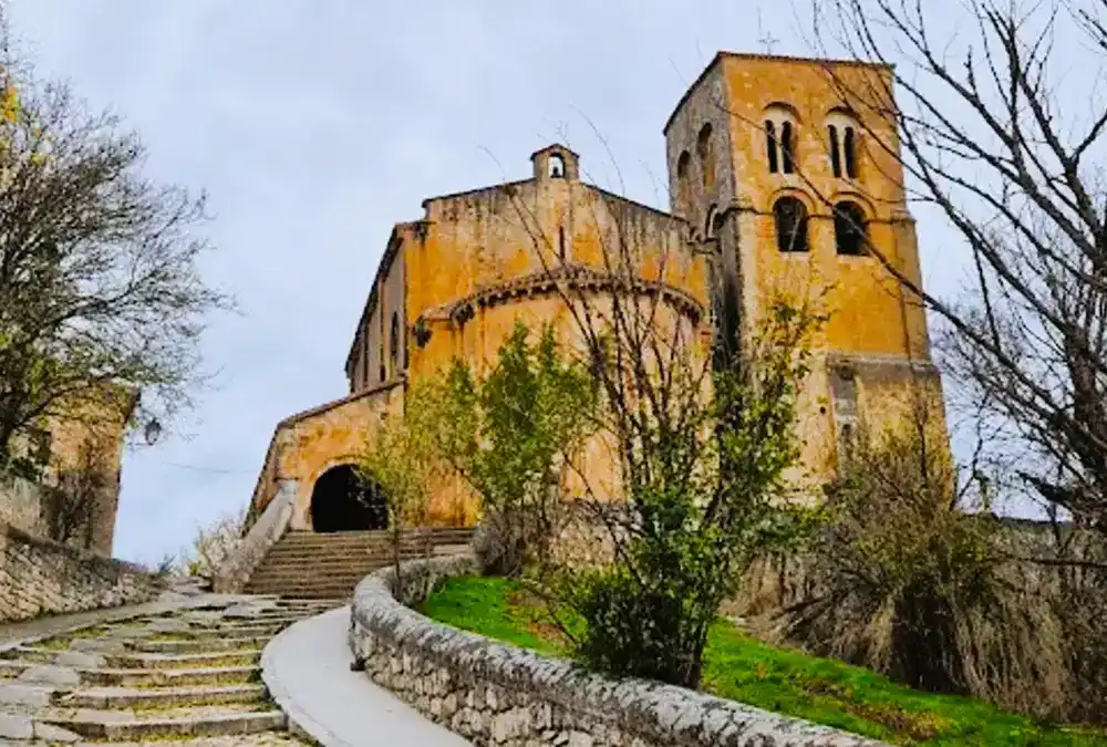Vista frontal e próxima da Igreja de San Salvador em Sepúlveda, mostrando o seu abside românico de pedra dourada, a torre sineira e uma escadaria de acesso que sobe a colina.