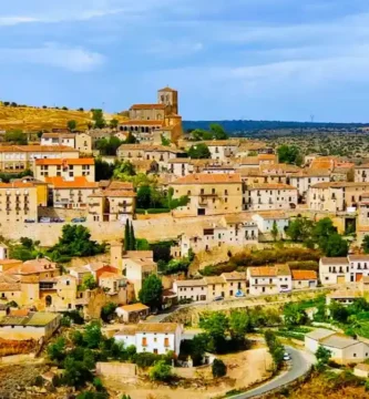 Uma vista panorâmica aérea da vila medieval de Sepúlveda, em Castela e Leão, Espanha, aninhada numa colina de pedra dourada com o desfiladeiro das Hoces del Duratón e campos rurais que se estendem ao fundo sob um céu nublado.