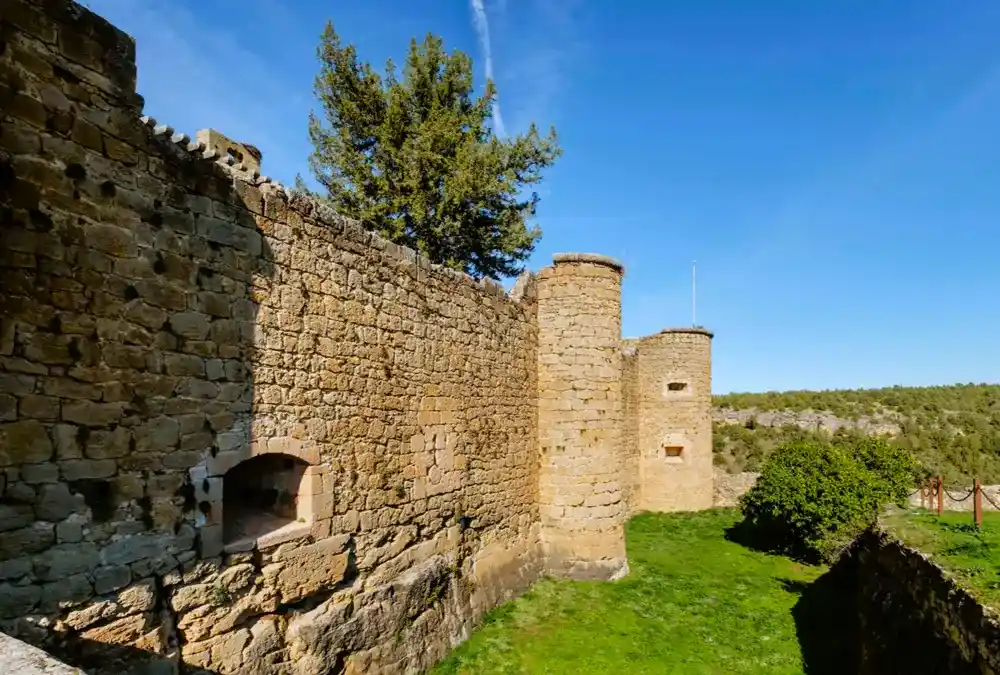 Vista lateral das robustas muralhas e torreões circulares do Castelo de Pedraza, construídos em alvenaria de pedra.