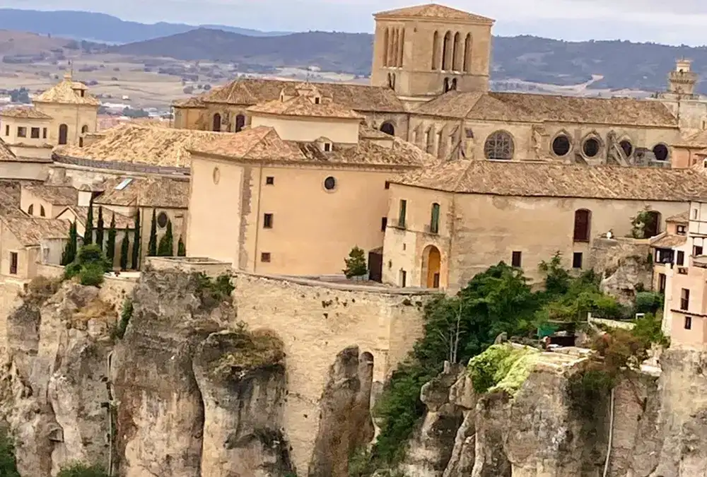 Vista panorâmica da zona antiga e edifícios históricos das Casas Colgadas de Cuenca, destacando a torre da catedral e construções no topo do penhasco.