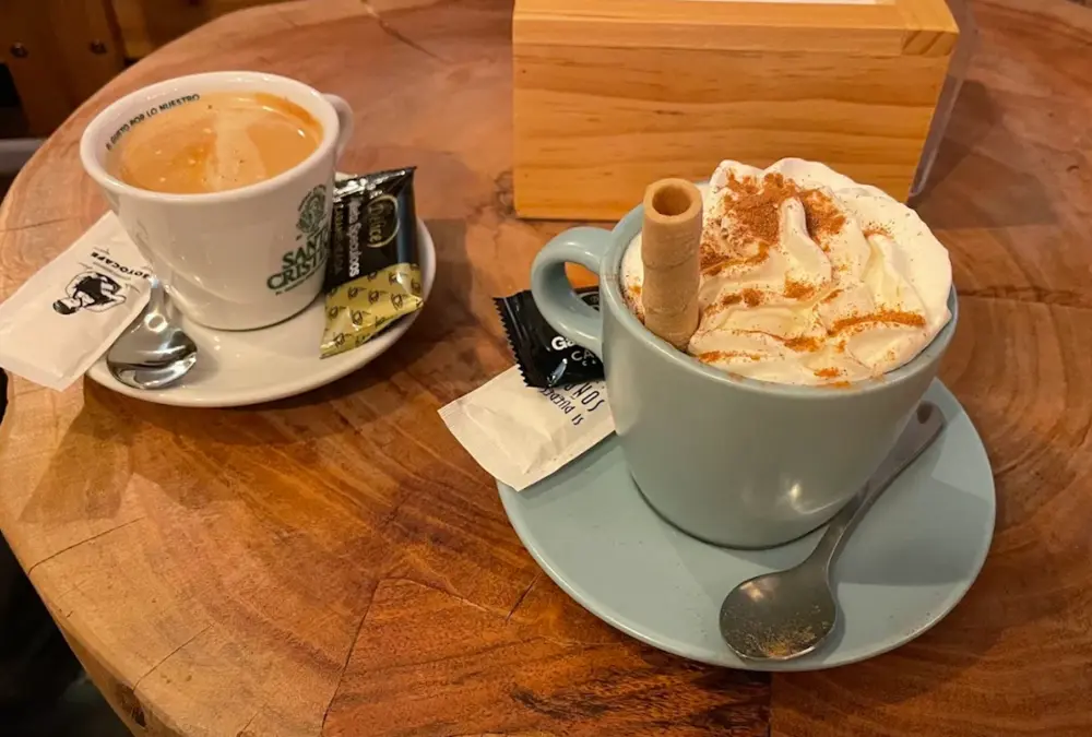 Chávenas de café expresso e café com natas e canela servidas sobre mesa de madeira rústica.
