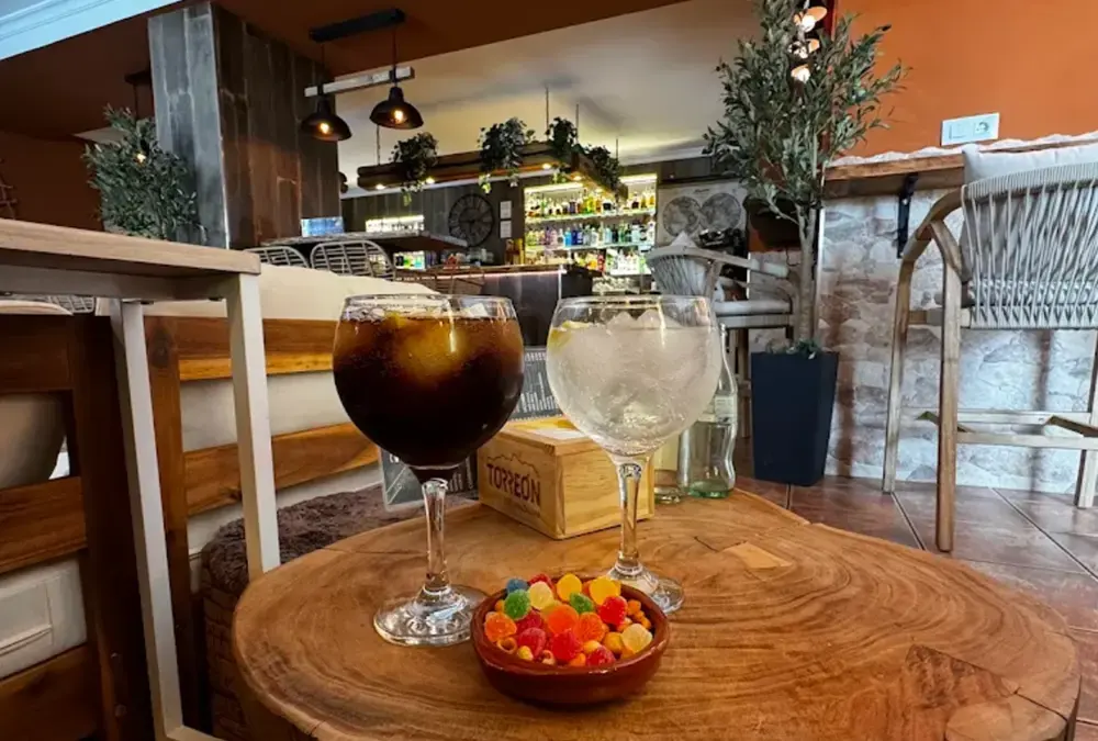 Mesa de madeira rústica em esplanada da Andaluzia com taças de bebidas e taça com doces.