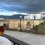 Cafés com Vista nas Cidades Brancas da Andaluzia: mesa de esplanada com taça de cerveja em primeiro plano e a Puente Nuevo de Ronda ao fundo.