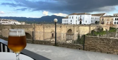 Cafés com Vista nas Cidades Brancas da Andaluzia: mesa de esplanada com taça de cerveja em primeiro plano e a Puente Nuevo de Ronda ao fundo.