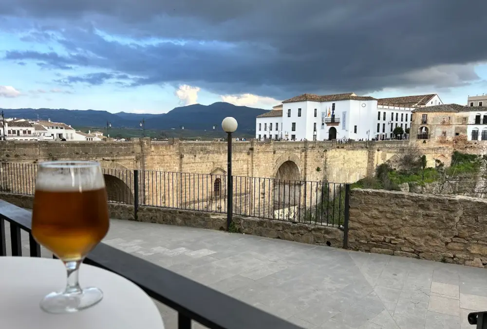 Cafés com Vista nas Cidades Brancas da Andaluzia: mesa de esplanada com taça de cerveja em primeiro plano e a Puente Nuevo de Ronda ao fundo.