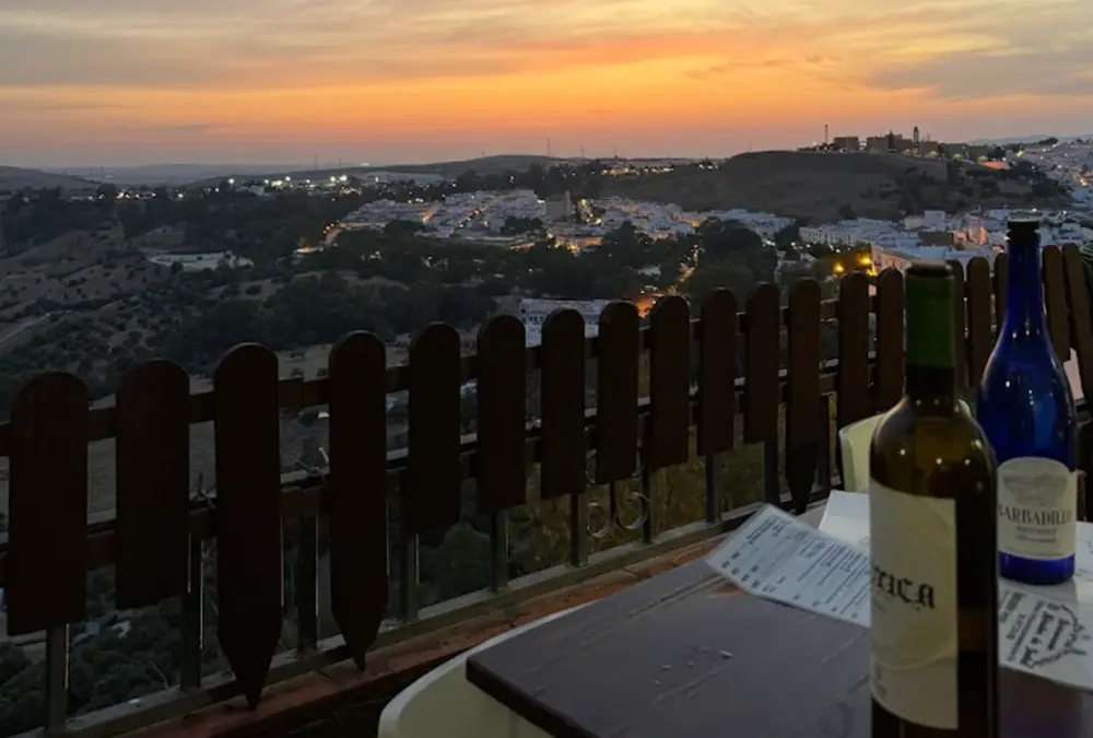 Garrafas de vinho em mesa de esplanada durante o pôr do sol com vista para o casario iluminado de Arcos de la Frontera.