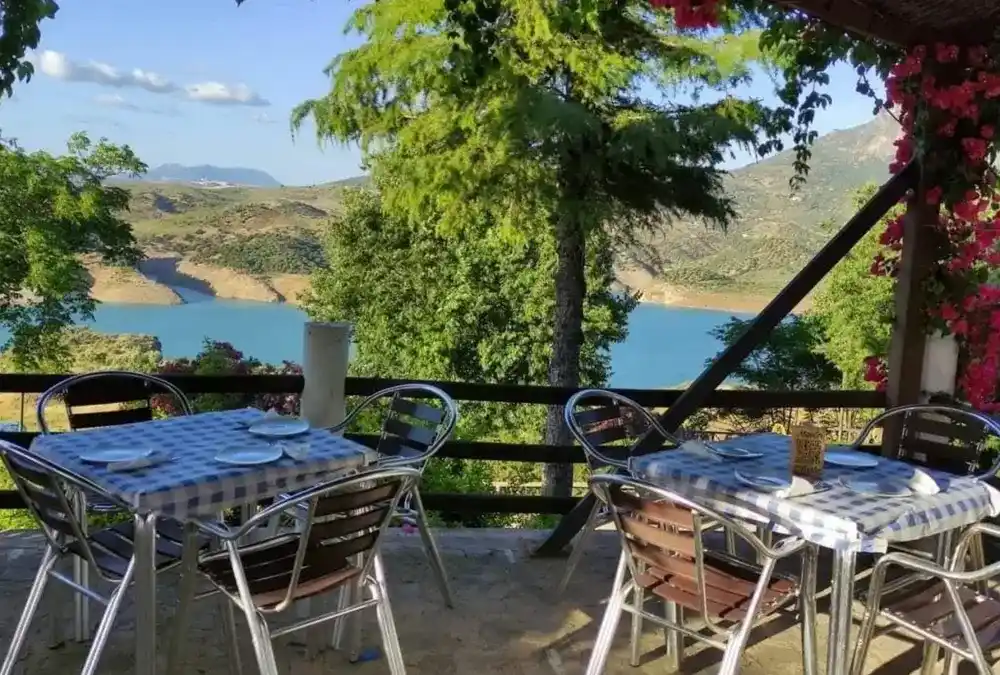 Mesas com toalhas aos quadradinhos azuis na varanda do Mesón Oñate com vista para a albufeira e montanhas de Zahara de la Sierra.