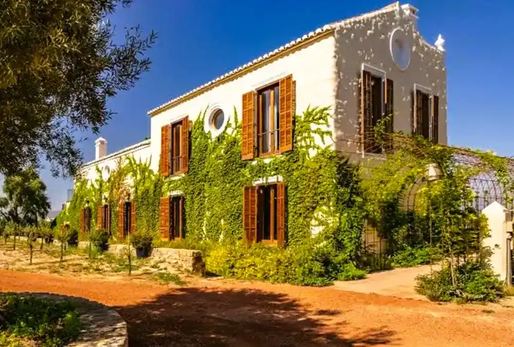Fachada de uma casa de campo senhorial branca coberta de hera verde com portadas de madeira castanha na Andaluzia.