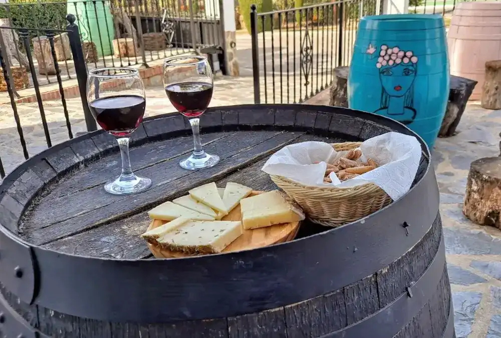 Tábua de queijos serranos cortados e dois copos de vinho tinto em cima de um barril de madeira antigo na esplanada.